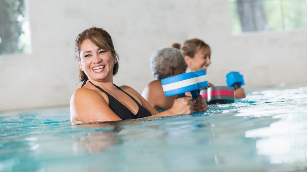 Group of adults participating in an aqua fitness class while exercising with water dumbbells in a swimming pool.