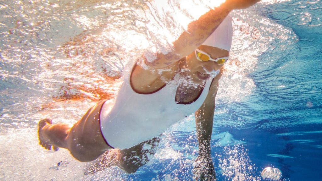 Competitive swimmer performing freestyle stroke underwater during swim training in a pool.