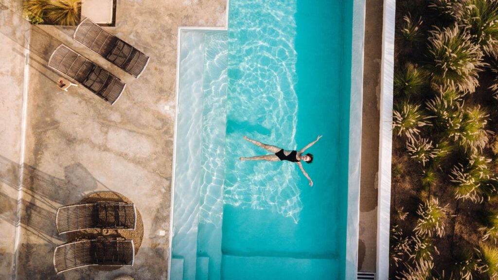 Woman performing a low-impact aqua fitness strength exercise in a swimming pool using aquatic resistance paddles.