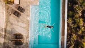 Woman performing a low-impact aqua fitness strength exercise in a swimming pool using aquatic resistance paddles.