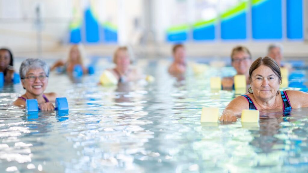 Older adults doing low-impact aqua fitness exercises with water dumbbells in a pool.