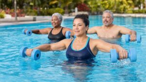 Three adults use aqua dumbbells during a water aerobics workout to strengthen the arms, shoulders, chest, back, and core.