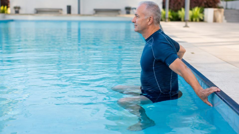 Man performing a supported knee-bend movement in a swimming pool during aquatic exercise for osteoarthritis.