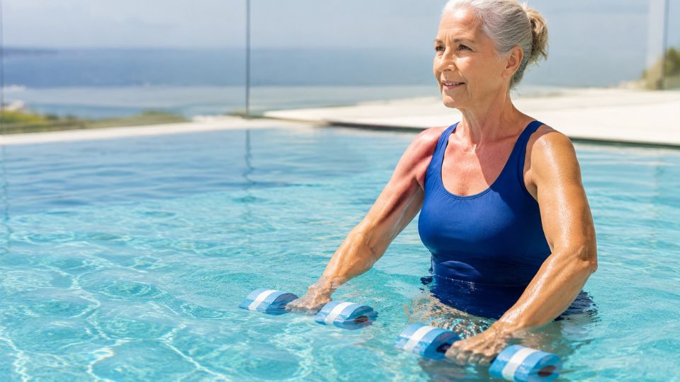 Woman using aqua dumbbells in a pool during water resistance training for bone health.